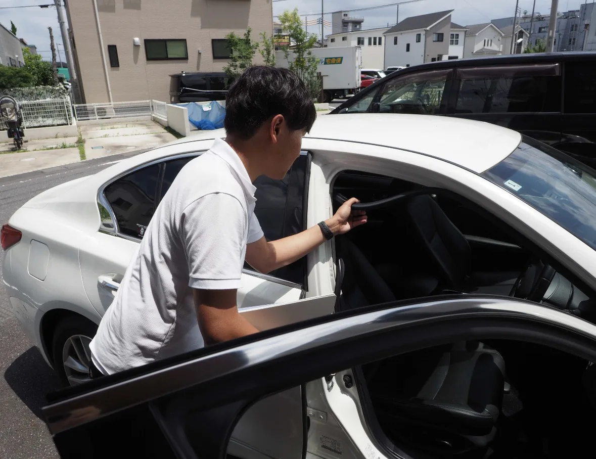白い車の後部座席を確認するLigare Cars（リガーレ カーズ）代表の中山