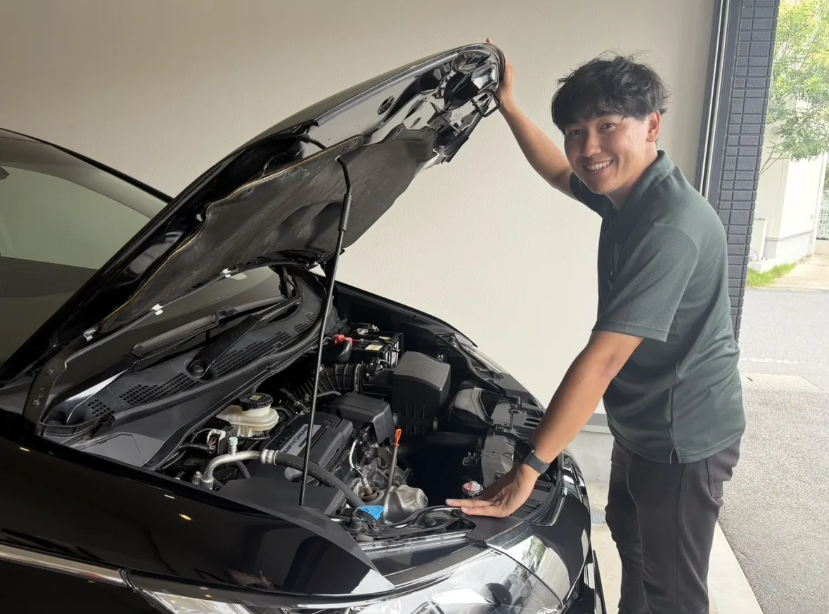 黒い車のボンネットを開けてエンジンルームを確認するLigare Cars(リガーレ カーズ)代表の中山